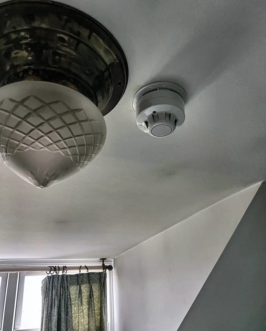 An optical smoke detector fitted beside a cut-glass ceiling light in a period room