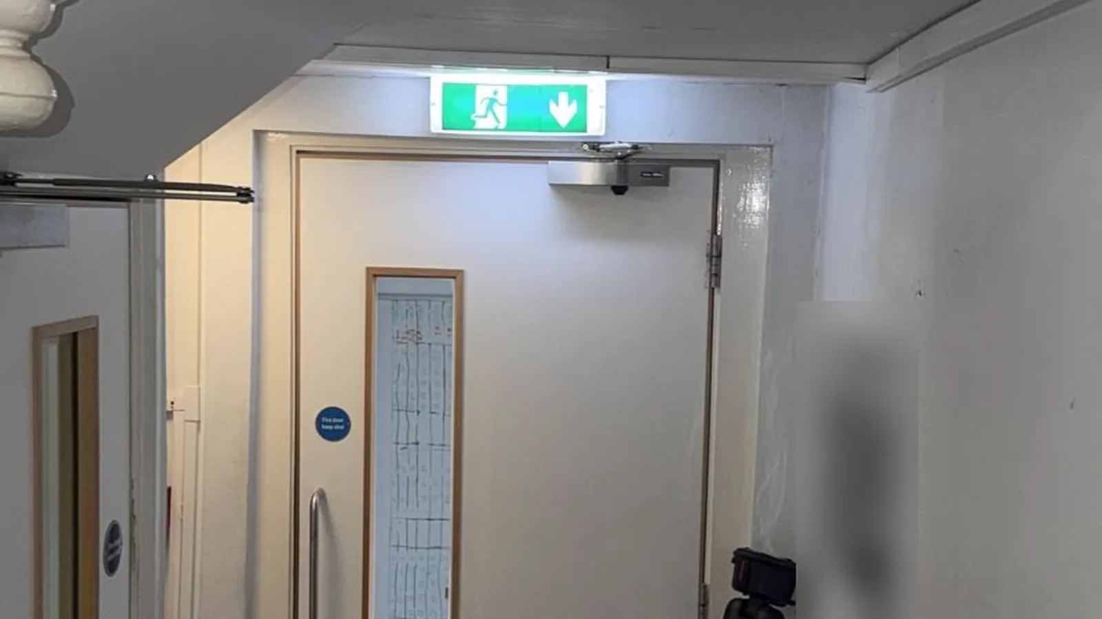 Fire risk assessment remedial works in London: a fire door with its closer and fire door keep shut sign, under an emergency exit sign, in an escape corridor